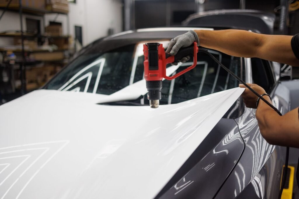 Installer using a heat gun to stretch white film over a car bonnet in a workshop