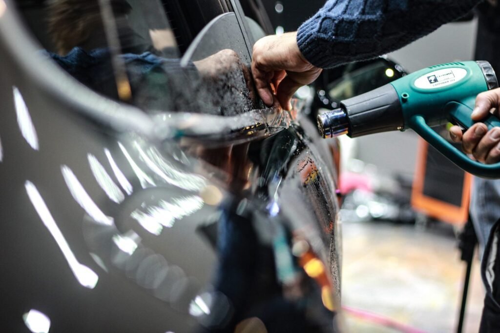 Hand lifting the edge of a film on a car door while a heat gun warms it