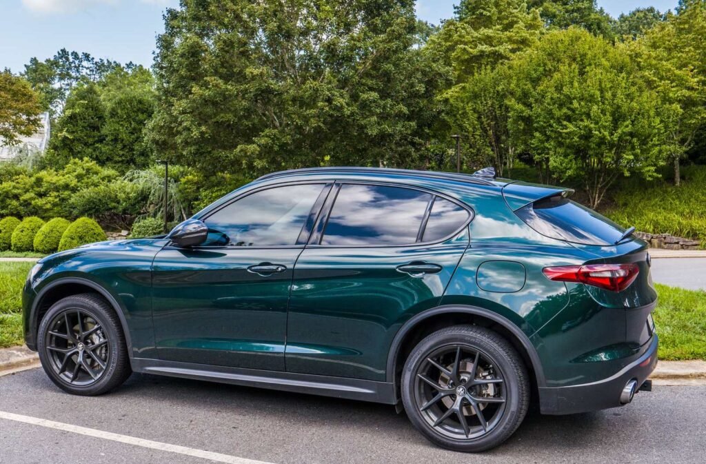 Green SUV with tinted side and rear windows parked beside a garden