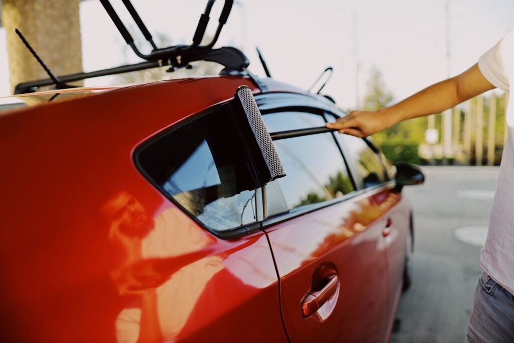Squeegee being drawn across the rear side window of a red hatchback